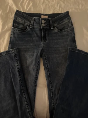 Mörkblå jeans från Nelly med detaljer - Snygga mörkblå jeans från Nelly med raka ben och dubbla knappar i midjan. Bakfickorna har coola vita zigzag-detaljer som sticker ut. Klassisk femficksmodell i stretchigt denimtyg som sitter skönt och passar till många olika stilar.