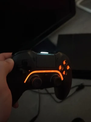 Svart PS4 handkontroll med LED-ljus - Snygg svart handkontroll till PS4 med orange LED-belysning runt touchpaden och knapparna. Kontrollen har klassisk PlayStation-layout med två styrspakar, styrkors och fyra knappar. Tillverkad i plast med en modern och ergonomisk form som passar perfekt för gaming.