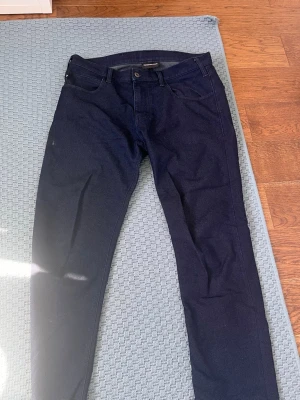 Mörkblå jeans från Emporio Armani - Snygga mörkblå jeans från Emporio Armani med klassisk femficksdesign och raka ben. Jeansen har en diskret logga på bakfickan och är tillverkade i ett mjukt denimtyg. Perfekta för en stilren och modern look. Jeansen passar perfekt för dem som är 173+ 
