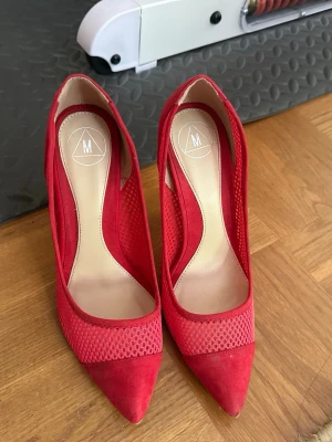Röda mesh-pumps med spetsig tå - Snygga röda pumps med spetsig tå och höga klackar. Skorna har mesh-detaljer på sidorna och mockaliknande material vid tån och hälen. Perfekta för dig som vill sticka ut med en färgstark look. Lite smutsiga på baksidan 