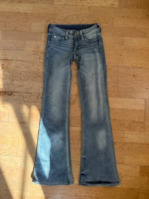 Cheap monday flare jeans💙💙 - Säljer ett par blå bootcut jeans med snygga slitningar och utsvängda ben. Jeansen har klassisk femficksdesign, knappgylf och en cool patch bak i midjan. Perfekta för dig som gillar retrostil och vill ha ett par jeans som sticker ut.