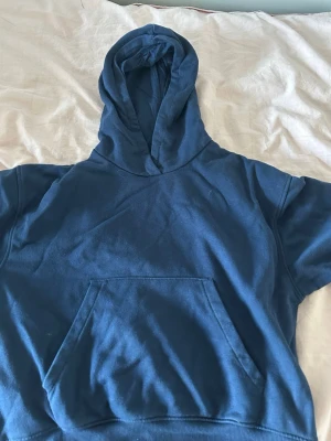 Mörkblå hoodie med magficka - En enkel och stilren mörkblå hoodie med stor huva och klassisk magficka framtill. Hoodien har ribbade muddar vid ärmslut och nederkant. Perfekt för en avslappnad look och passar till det mesta. Materialet känns mjukt och bekvämt.