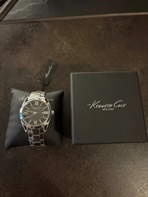 Kenneth Cole klocka - Säljer denna helt oanvända klocka åt min morfar. Klockan kommer från ett lager efter en nedlagd klockbutik och har aldrig använts.  * Skick: Ny/oanvänd * Funktion: Klockan saknar batteri, vilket köparen själv får ordna. * Box och tagg medföljer vid köp. * Nypris: cirka 2 000 kr.  Klockan säljs privat och kan skickas eller hämtas efter överenskommelse. Fler bilder kan skickas vid intresse.  Pris kan diskuteras vid snabb affär.