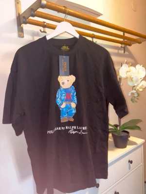 Svart Polo Bear t-shirt Ralph Lauren - Svart t-shirt från Ralph Lauren med ikoniska Polo Bear-trycket . Kommer i storlek Xl men passar även dess med storlek M/L som gillar det lite baggy. 