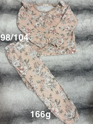 Blommig pyjamas  - Supersöt tvådelad pyjamas med blommigt mönster. Tröjan har volangdetaljer vid axlarna och byxorna har resår i midjan för extra komfort. Perfekt för mysiga kvällar hemma.🌸 Fint använt skick. Storlek 98/104