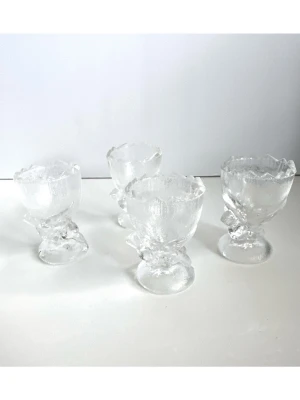 4 äggkoppar i glas med fågelmotiv  - Härligt set med fyra äggkoppar med fågelmotiv i glas. Vacker texturernas yta och en dekorativ sicksack-kant upptill. Rund fot med liten fågel-figurin under varje äggkopp. Unika äggkoppar som kommer förgylla varje morgon. 7cm höga. Mycket gott skick!