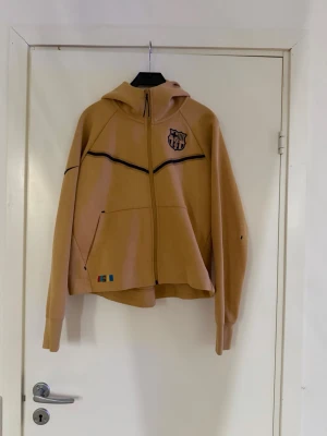 FC Barcelona hoodie med dragkedja - Säljer en beige/senapsgul hoodie med FC Barcelona-logga på bröstet och svarta detaljer. Hoodien har dragkedja framtill, två fickor och en huva. Aldrig använd! Passar absolut en XS!😊