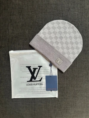 Grå mössa med mönster - Snygg grå mössa med klassiskt rutmönster och vikt kant. Logga på en patch framtill. Tillverkad i mjukt material som känns lyxigt och stilrent. Perfekt accessoar för dig som vill ha något exklusivt och trendigt. Aldrig använd.