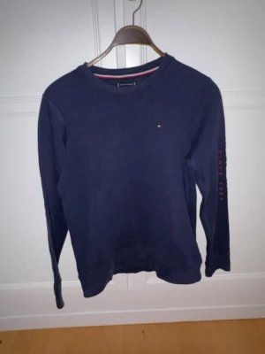 Mörkblå tröja Tommy hilfiger - Mörkblå långärmad tröja med rund halsringning och diskret logga på bröstet. Perfekt för en avslappnad stil. Passar dig med storlek 176-XS