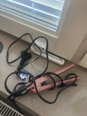 Rosa miniplatång  - Säljer en rosa plattång med svart sladd. Plattången har en smal och avlång form, perfekt för att styla med. Enkel att använda och passar bra för dig som vill fixa frisyren snabbt.