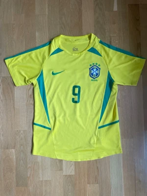 Brasilien VM 2002 hemmatröja - Brasilien hemmatröja från VM 2002 med Ronaldo #9 på ryggen. Mycket bra skick utan skador. Klassisk och ikonisk tröja från Brasiliens VM-guld, perfekt för samlare eller fotbollsfans.