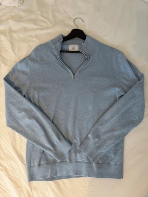 Ljusblå half zip tröja från Bläck - Snygg ljusblå tröja från Bläck med half zip-dragkedja. Perfekt för dig som gillar en enkel men stilren look. Tröjan har lång ärm och är tillverkad i mjukt material som känns skönt mot huden.