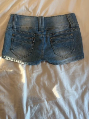 Blå denimshorts med dragkedjedetalj - Säljer ett par blå denimshorts med två knappar framtill, dragkedjedetalj på ena fickan och klassiska bakfickor. Midjemått: 39cm, Gren: 20cm