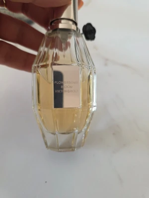 Flowerbomb Bloom parfym Viktor & Rolf - Flowerbomb Bloom från Viktor & Rolf i en elegant, multifasetterad glasflaska med ljusgul vätska. Flaskan har en silverfärgad metallkork och en svart blomdetalj vid halsen. Perfekt för dig som gillar blommiga och fräscha dofter.