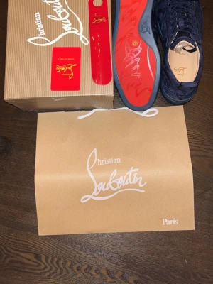 Mörkblå sneakers från Christian Louboutin - Snygga mörkblå sneakers från Christian Louboutin i mocka med klassisk röd sula och diskret logga på sidan. Skorna har rund tå, matchande mörkblå snörning och en stilren design som sticker ut med den ikoniska röda undersidan.