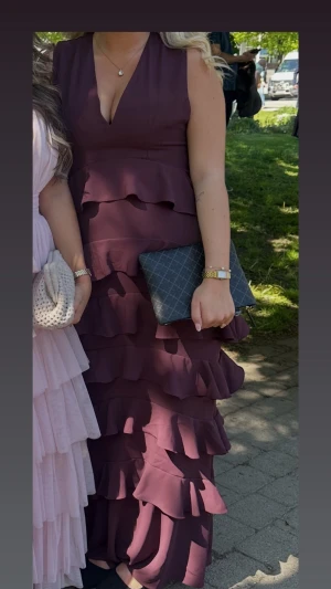 Vinröd långklänning med volanger - Säljer min balklänning, den är i super fint skick. Den har en ganska djup v-ringning fram och bak (skriv privat för fler bilder baktill) perfekt för bröllop eller bal eller en dag du vill va extra uppklädd 