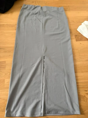 Ljusgrå lång kjol med slits - Säljer en stilren ljusgrå lång kjol med rak passform och slits baktill. Kjolen är i ett mjukt, stretchigt material som ger en bekväm känsla och passar perfekt till många olika looks.