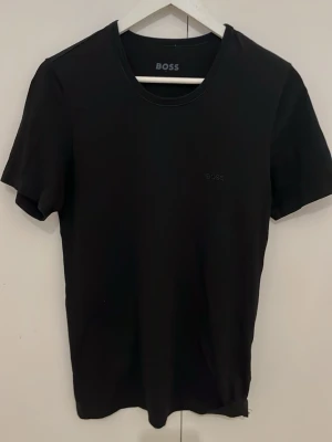 Svart t-shirt från BOSS - Snygg svart t-shirt från BOSS med diskret logga på bröstet. Klassisk rund halsringning och korta ärmar. Perfekt basplagg som funkar till allt och är enkel att matcha. Tillverkad i mjukt material för skön känsla.