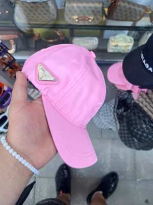 TOPP keps   - Snygg rosa keps från med det ikoniska metalltriangel-logotypen på sidan. Kepsen har böjd skärm och är tillverkad i ett glansigt, lätt material som ger en modern och trendig look. Perfekt accessoar för att lyfta din outfit.