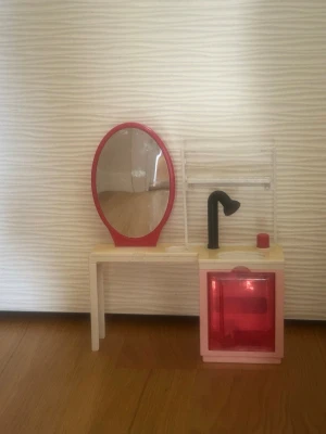 Dockhusmöbel sminkbord och handfat - Säljer ett frisörbord med  handfat, vattenpump,kran och en frisörstol för Barbie dockor. Bordet har en oval spegel med röd ram, svart kran och ett underskåp med röd lucka där man fyller med vatten . Perfekt tillbehör till barn som gillar att leka med Barbies . Bordet är gult och detaljerna är i rött och svart. med en vit hylla där din Barbies hårprodukter kan stå.