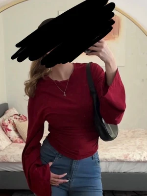 Röd långärmad topp med vida ärmar - Säljer en snygg röd topp med långa, vida ärmar och figurnära passform. Toppen har rund halsringning och är lätt croppad i modellen. Perfekt att styla med jeans eller kjol för en trendig look.