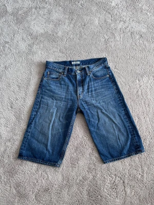 Blå denimshorts  - Säljer ett par klassiska blå denimshorts med fem fickor och normalhög midja. Shortsen har raka ben och stängs med dragkedja och knapp. Perfekta för en avslappnad stil och tillverkade i slitstarkt jeanstyg.