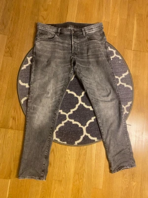 G-Star RAW jeans i grå wash Mycket fint skick -  Säljer ett par stilrena G-Star RAW Tapered Jeans i snygg grå wash, storlek 34/32. Köpta direkt i G-Star RAW-butik för 1 200 kr.  Modellen har Tapered Fit, vilket innebär att jeansen är något rymligare upptill och smalnar av nedåt för en modern och bekväm passform.  Jeansen är endast använda ett fåtal gånger och är i mycket fint skick. Det finns ett litet hål i grenen, men det är enkelt att sy ihop själv eller lämna in till skräddare för en billig lagning.I övrigt är jeansen väldigt fräscha.