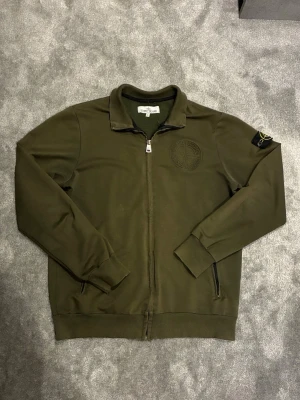 Olivgrön ziptröja från Stone Island - Säljer en olivgrön ziptröja från Stone Island med klassisk patch på ärmen och diskret broderad logga på bröstet. Tröjan har ribbade muddar, ståkrage och två fickor med dragkedja. Perfekt för streetwear men även för mer formella sammanhang. Storleken är XL men den har passat mig som är L och M perfekt ändå. Priset kan diskuteras.