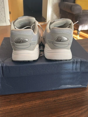 Gråa sneakers med CD-detalj - Snygga sneakers i ljusgrått med CD-logga på hälen. Skorna har en chunky sula och är tillverkade i mesh och syntetmaterial för en sportig look. Perfekta för dig som gillar stilrena och moderna sneakers.
