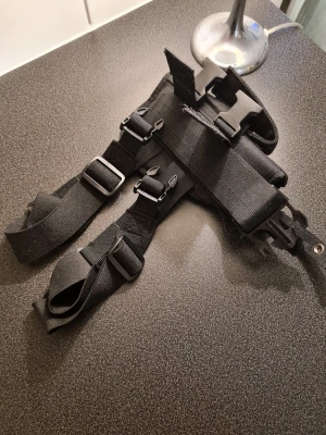 Svart taktisk axelhölster - Säljer ett svart taktiskt axelhölster med justerbara remmar och flera spännen. Tillverkat i slitstark nylon med kardborreband och snabbfästen. Perfekt för dig som vill ha en cool och funktionell accessoar till din outfit.