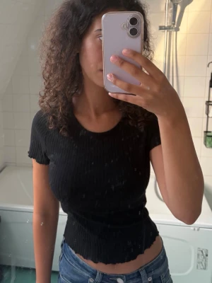 Svart ribbad croppad topp - Säljer en svart ribbad topp med korta ärmar och croppad passform, perfekt till en enkel men snygg look.