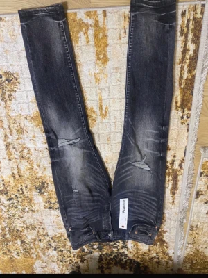 Svarta ripped jeans från Purple Brand - Säljer ett par svarta skinny jeans från Purple Brand med slitningar och distressed detaljer på benen. Jeansen har klassisk femficksmodell och knappgylf. Materialet är denim med stretch för extra komfort. Perfekta för en trendig och avslappnad look.