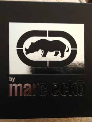 Marc Eckō - Stilren klocka från Marc Ecko med svart läderband och silverfärgat boett. Baksidan har en graverad döskalle med krona och detaljer runtom. Klockan har en klassisk rund form och passar perfekt för dig som gillar streetwear och unika detaljer. Det ligger också en gåva med i boxen från designern i form av ett moneyclip . Till köparen av klockan kommer en amerikansk dollar sedel följa med (samla mynt sedlar förr ) och just denna sedeln är helt oviken och felfri så detta money clip passar perfekt 😆