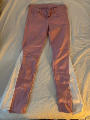 Rosa jeans med vita utsvängda ben - Unika rosa jeans med vita tygpaneler längs utsidan av benen som ger en cool utsvängd effekt. Modellen är slim fit upptill och blir bredare nedtill. Klassisk femficksdesign och knappgylf. Perfekta för dig som vill sticka ut med din stil.