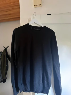 Svart stickad tröja J.Lindeberg - Klassisk svart stickad tröja från J.Lindeberg med rund halsringning och ribbade muddar vid ärmslut och nederkant. Enkel och stilren design som passar till det mesta. Perfekt basplagg för garderoben.
