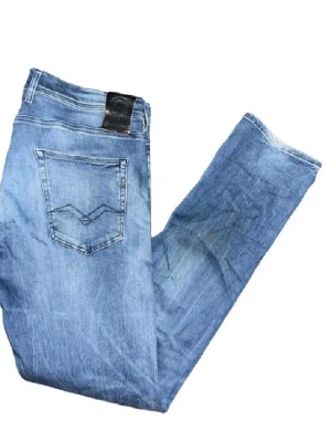 Replay Grover jeans  - Säljer ett par Replay Grover jeans i ljusblå tvätt med klassisk femficksdesign och snygga slitningar. Jeansen har raka ben och normal passform, med Replay-logga på bakfickan och läderpatch i midjan. Perfekta för dig som gillar en avslappnad stil. Midja 45cm, längd 107cm OBS, jeansen har fläckar som syns på en utav bilderna och även har lite fåll alltså slitningar längst ned på benen på baksifan :)
