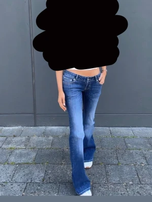 Blå bootcut jeans med låg midja - Säljer ett par blå bootcut jeans med låg midja och slitna detaljer. Jeansen har klassisk femficksmodell och är tillverkade i denim med lätt stretch. Säljer pga ingen användning 
