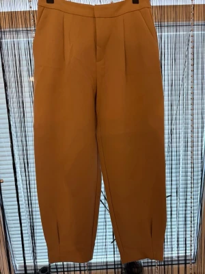 Beige kostymbyxor med pressveck - Snygga beige kostymbyxor med hög midja och raka ben. Byxorna har pressveck framtill, diskreta fickor och stängs med dold dragkedja. Materialet ser ut att vara mjukt och lite stretchigt, perfekt för en clean och stilren look.