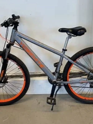 Grå-orange mountainbike - Säljer en grå mountainbike med orangea detaljer och text på ramen. Cykeln har svart sadel, svarta handtag och orangea fälgar. Utrustad med grova däck och framgaffel med stötdämpare. Perfekt för dig som gillar att cykla i terräng.