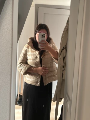 Beige Herno jacka Sofia - Säljer en beigeHerno, kort pufferjacka med hög krage . Modell Sofia. Jackan har en boxig passform och stängs med knappar framtill. Fint skick förutom en arm som fått lite svarta märken. Kan nog gå bort på kemtvätt inte testat. Vet inte storlek tror det är typ en medium.