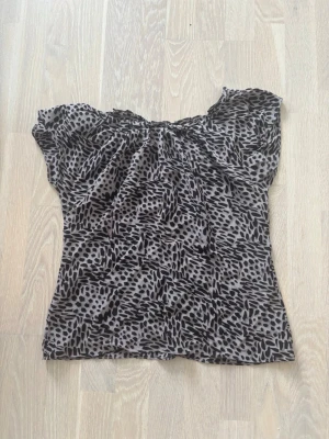 Topp med svart leopardmönster - Snygg topp med svart leopardmönster mönster och korta ärmar. Toppen har en lös passform och är gjord i ett tunt, lätt material som känns luftigt. Perfekt för dig som gillar en unik och trendig stil. Storlek XS/S