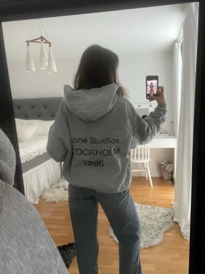 Grå hoodie Acne Studios Stockholm - Säljer en grå hoodie från Acne Studios med tryck på ryggen där det står 'Acne Studios STOCKHOLM 1996'. Hoodien har en klassisk passform, huva och långa ärmar. Perfekt för en chill och avslappnad stil. Köpt på Vinted🩷