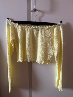 Gul cropp topp från BikBok - Säljer en ljusgul offshoulder topp från BikBok i storlek M. Toppen har lång ärm, smockat tyg och en croppad passform. Plagget är i mycket bra skick. Perfekt för dig som vill ha en söt och trendig topp till sommaren!