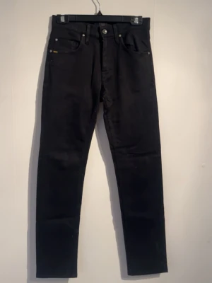Svarta slim jeans från tiger of sweden - Säljer ett par svarta slim jeans från tiger of sweden och klassisk femficksdesign. Jeansen har smal passform och raka ben, perfekta till en trendig och clean look. 