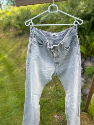 Ljusgrå raka jeans - Säljer ett par ljusgrå jeans med klassisk femficksdesign och raka ben. Jeansen har en enkel look utan synliga slitningar eller dekorationer, och är tillverkade i ett mjukt denimtyg. Perfekta för en avslappnad stil.