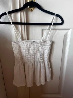 Vit smockad topp med tunna axelband - Supersöt vit topp med smockad överdel och tunna axelband. Toppen har avtagbara axelband och går även att ha som kjol! Storlek xs och ifrån gina tricot. Fint skick❣️❣️