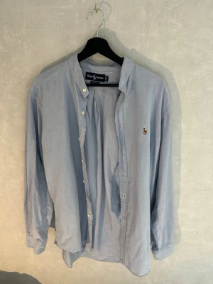 Ljusblå skjorta från Ralph Lauren - Klassisk ljusblå skjorta från Ralph Lauren med button-down krage och broderad logga på bröstet. Skjortan har långa ärmar, vita knappar och är tillverkad i mjuk bomull. Perfekt för en avslappnad men ändå stilren look. Vi kommer att fixa det som har gått sönder!