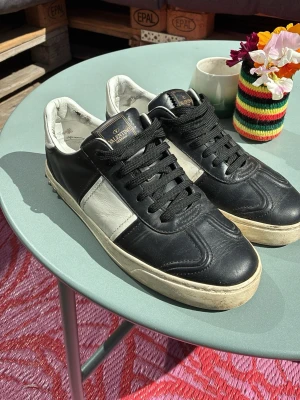 Svarta och vita sneakers från Valentino - Snygga sneakers från Valentino i svart och vitt läder med klassisk låg siluett. Skorna har svarta snören, vit sula och diskret Valentino-logga på plösen. Perfekta för dig som vill ha en stilren och exklusiv look.