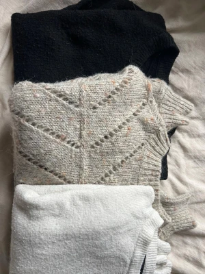 Tre stickade tröjor i olika färger - Säljer tre stickade tröjor: en svart, en ljusgråmelerad med hålmönster och små färgprickar samt en vit. Alla har rund hals och lång ärm💗