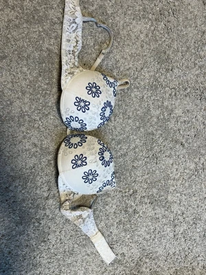 Intimissimi bh - Säljer en vit bh med blått blommönster och vadderade kupor. Axelbanden och sidorna har fina spetsdetaljer. Bh:n har hakknäppning bak och justerbara axelband för bästa passform. Materialet är mjukt och bekvämt. Är inte helt säker på storleken, men skriv om du vill ha mått